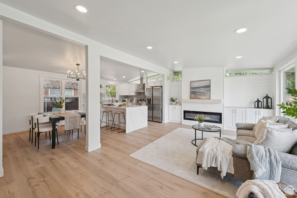 Living area featuring a chandelier, a glass covered fireplace, recessed lighting, light wood-style floors, and baseboards