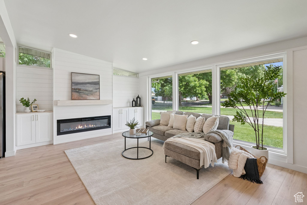 Living area featuring light wood-style floors, a glass covered fireplace, healthy amount of natural light, and recessed lighting