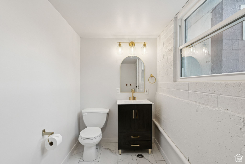Bathroom with toilet, vanity, marble look tile flooring, and baseboards