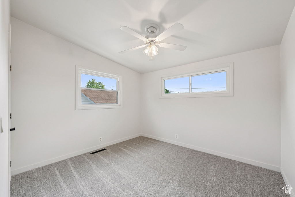 Unfurnished room featuring light colored carpet, vaulted ceiling, baseboards, and ceiling fan