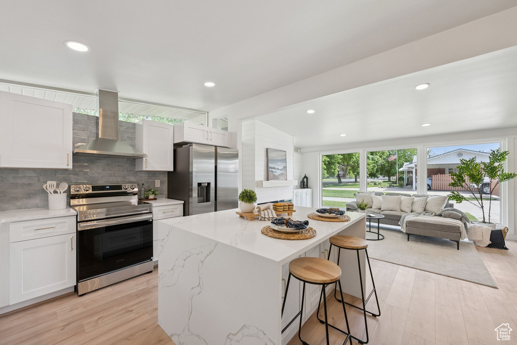 Kitchen featuring stainless steel appliances, wall chimney exhaust hood, a kitchen bar, a kitchen island, and white cabinets