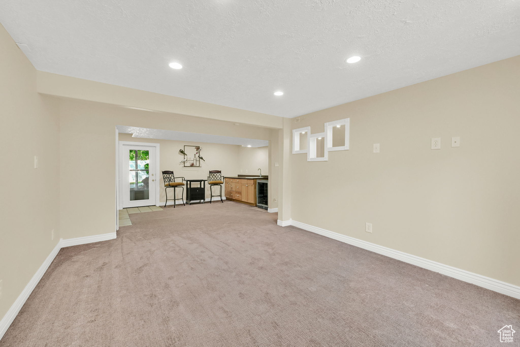 Unfurnished living room with wine cooler, light carpet, baseboards, recessed lighting, and wet bar