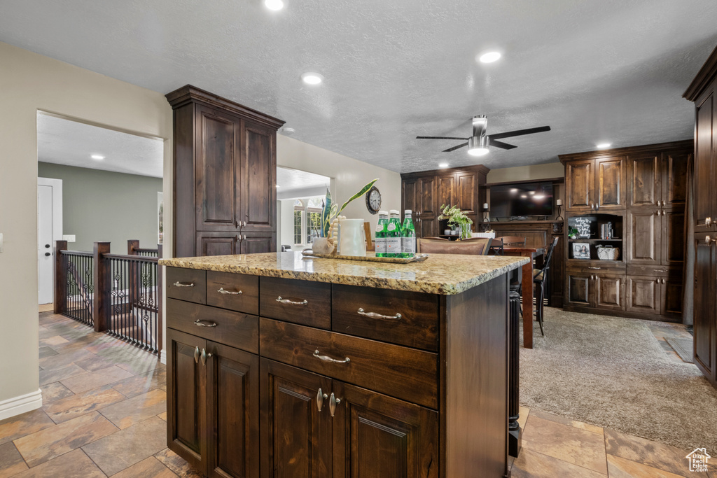 Kitchen featuring a ceiling fan, dark brown cabinets, a center island, light stone counters, and recessed lighting