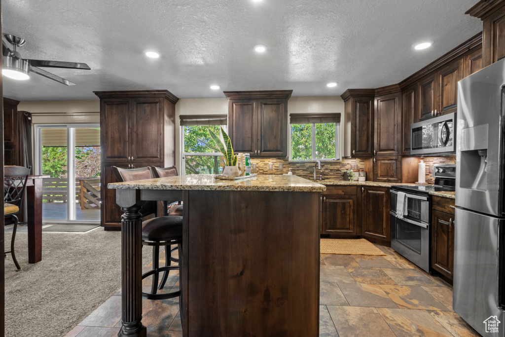 Kitchen featuring stainless steel appliances, a center island, a kitchen breakfast bar, dark brown cabinets, and backsplash