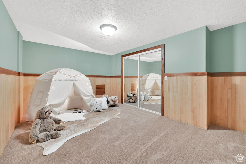 Carpeted bedroom with a textured ceiling, a wainscoted wall, wood walls, and a closet