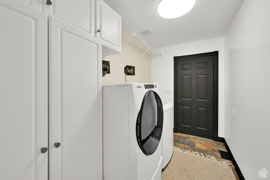 Washroom with baseboards, washer and clothes dryer, cabinet space, and light stone finish floors