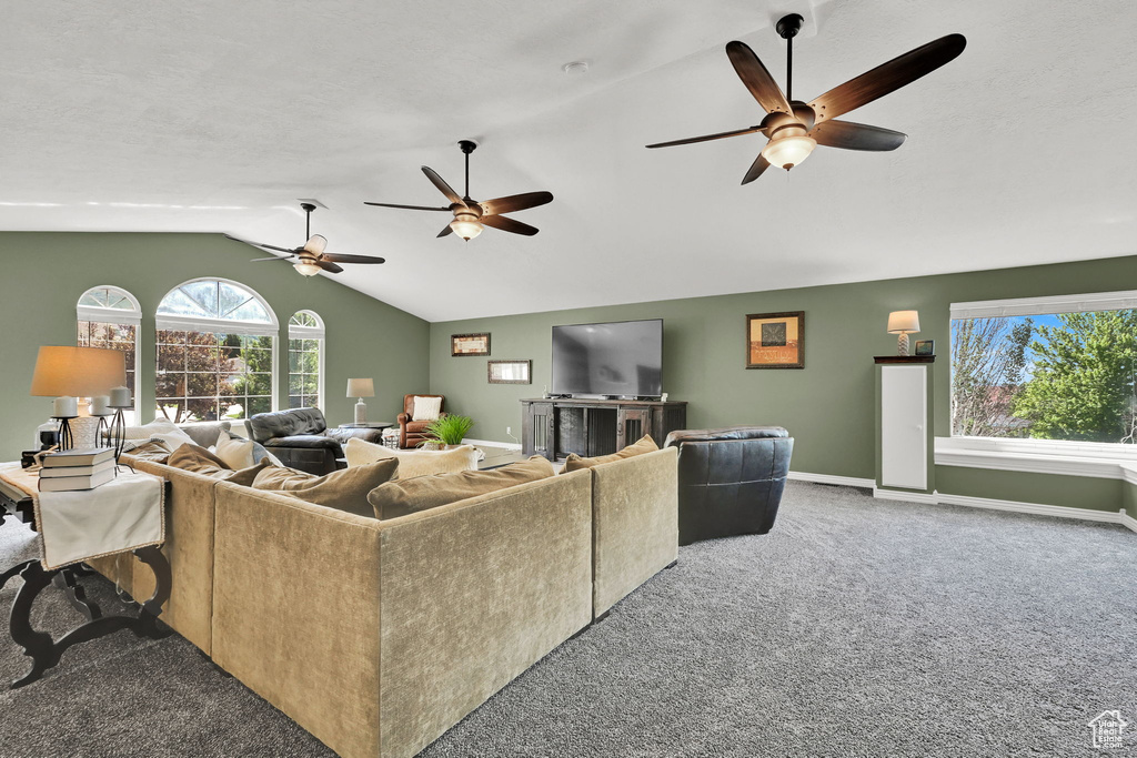 Carpeted living room with vaulted ceiling, plenty of natural light, ceiling fan, and baseboards