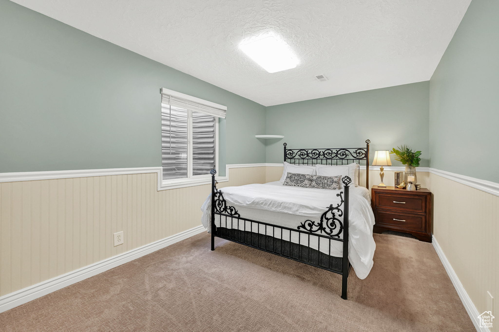 Carpeted bedroom featuring wainscoting, a textured ceiling, and baseboards