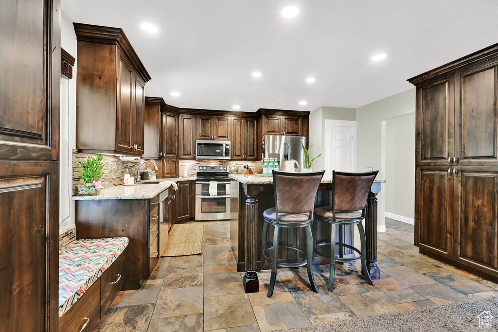Kitchen featuring stainless steel appliances, stone tile floors, dark brown cabinetry, decorative backsplash, and recessed lighting