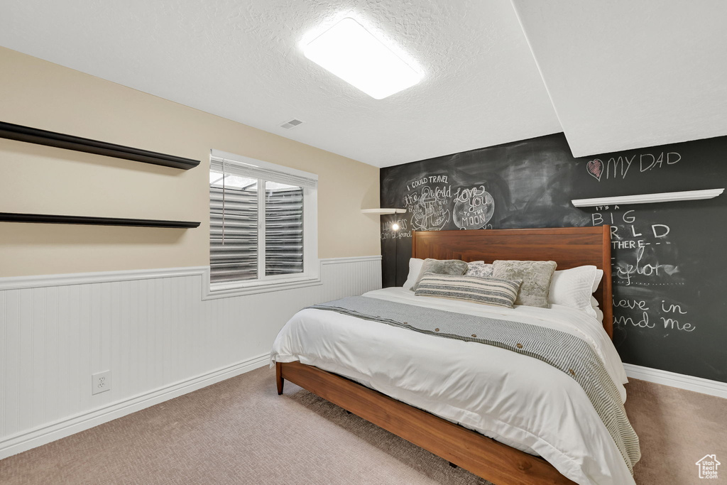 Carpeted bedroom featuring wainscoting, a textured ceiling, and baseboards