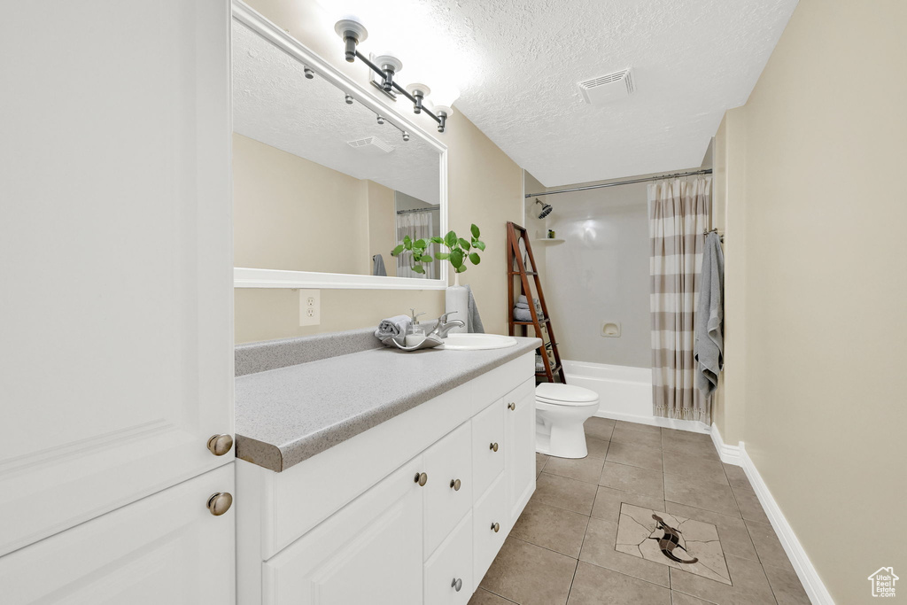 Bathroom featuring vanity, tile patterned floors, toilet, shower / tub combo with curtain, and a textured ceiling