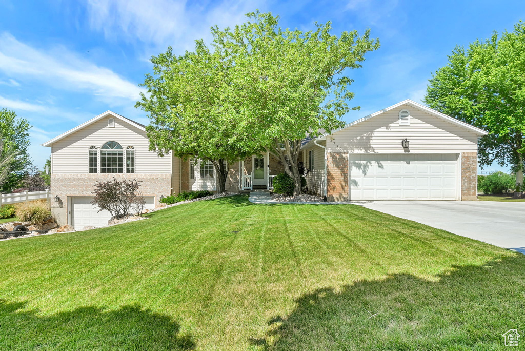View of front of house featuring concrete driveway, brick siding, a front lawn, and an attached garage