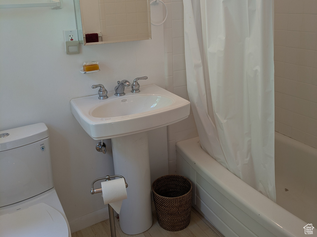 Full bath featuring shower / bath combo with shower curtain, wood finished floors, toilet, and a sink
