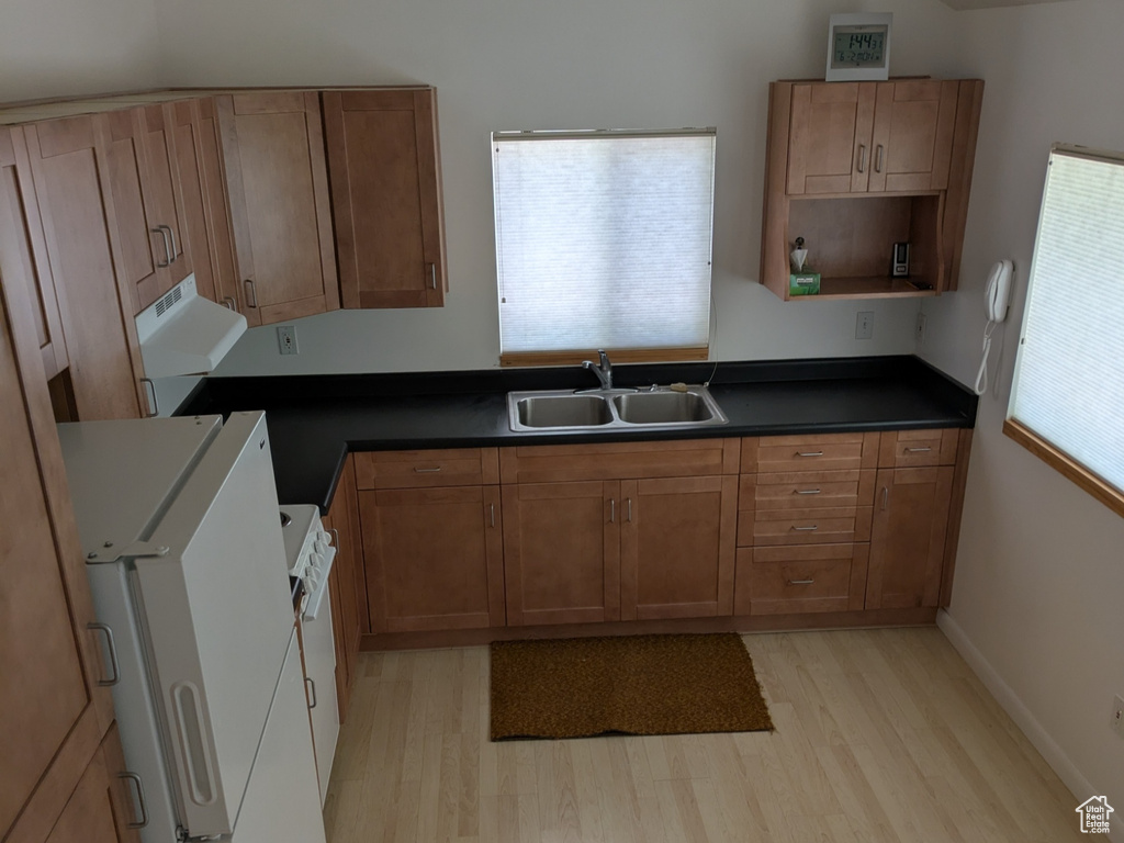 Kitchen featuring a sink, lofted ceiling, freestanding refrigerator, light wood-style floors, and dark countertops