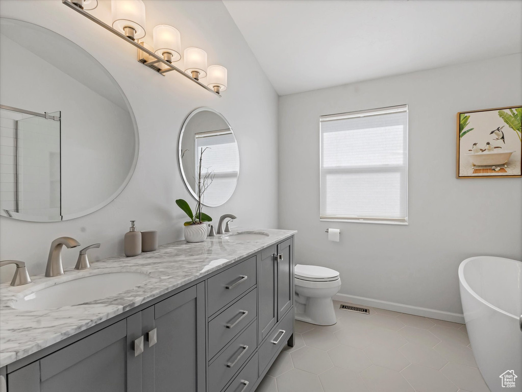 Bathroom with double vanity, a freestanding tub, toilet, lofted ceiling, and tile patterned flooring