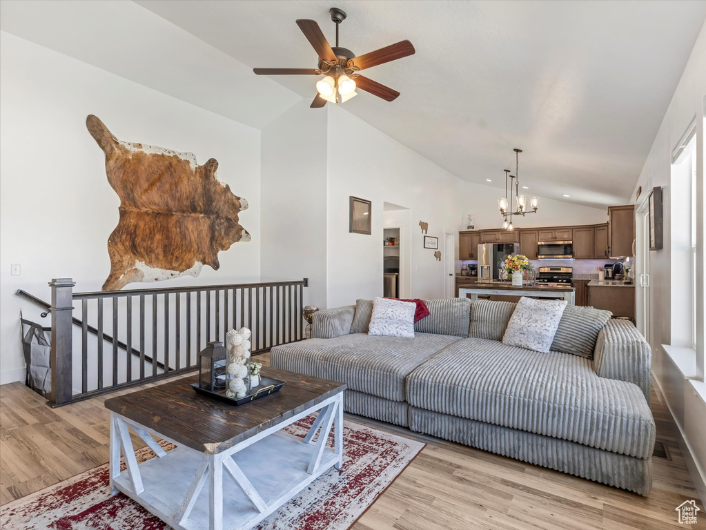 Living room featuring vaulted ceiling, light wood-type flooring, a ceiling fan, and a chandelier