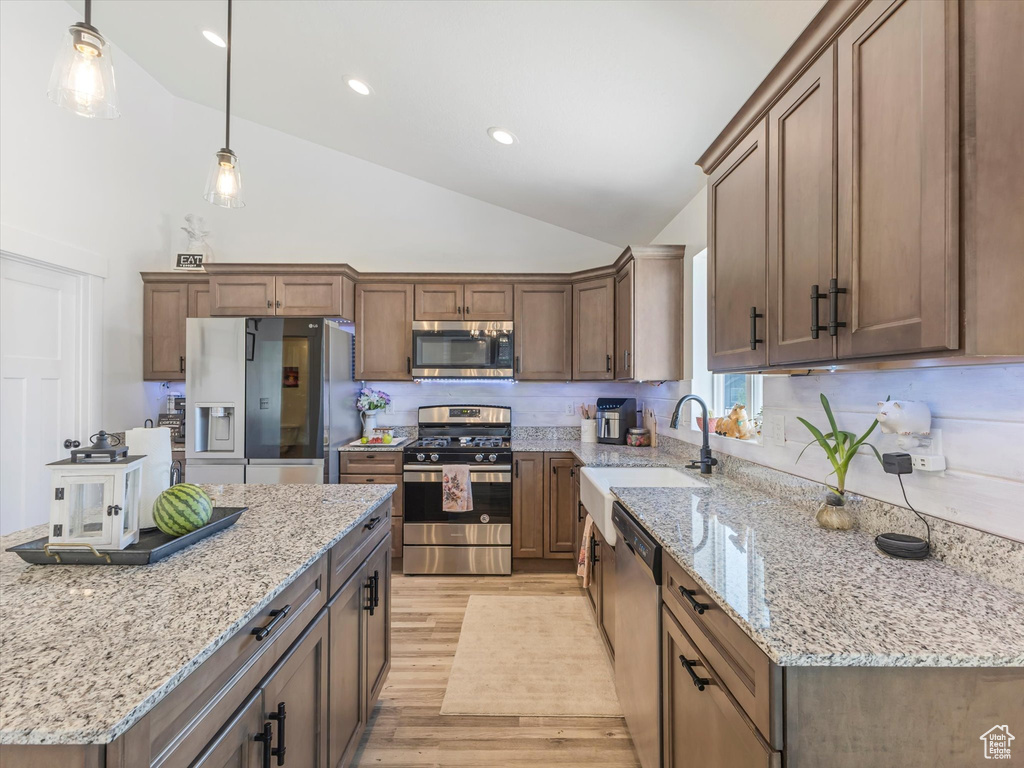 Kitchen with stainless steel appliances, light wood finished floors, a sink, high vaulted ceiling, and decorative light fixtures