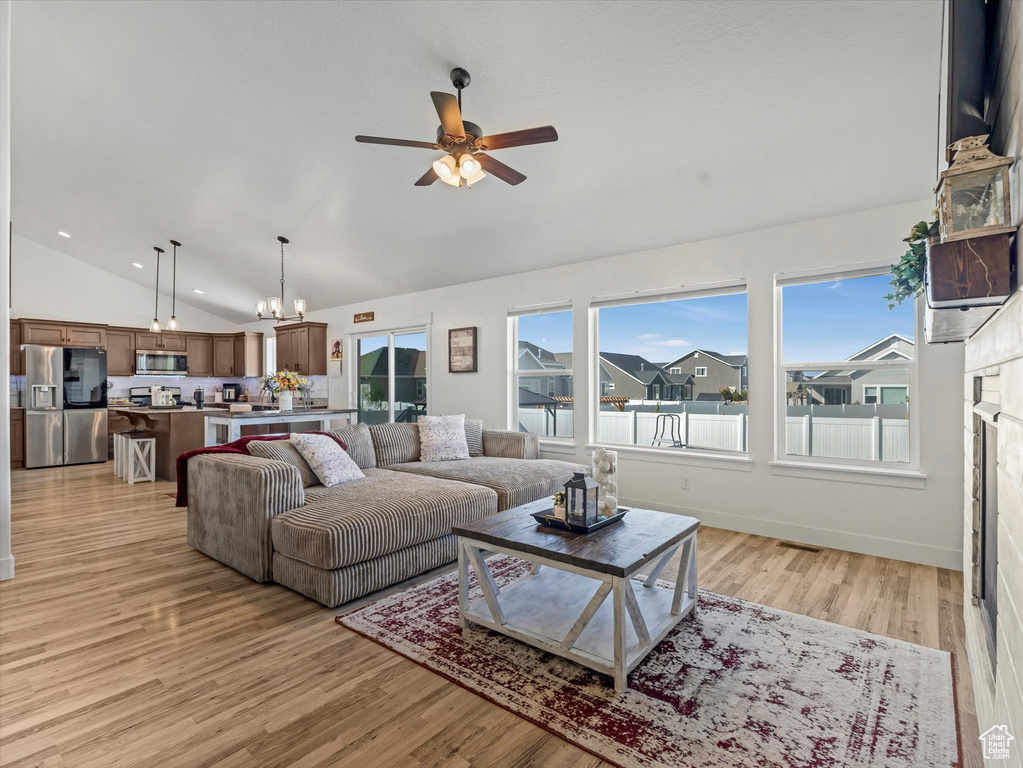 Living area with vaulted ceiling, ceiling fan, a chandelier, and light wood finished floors