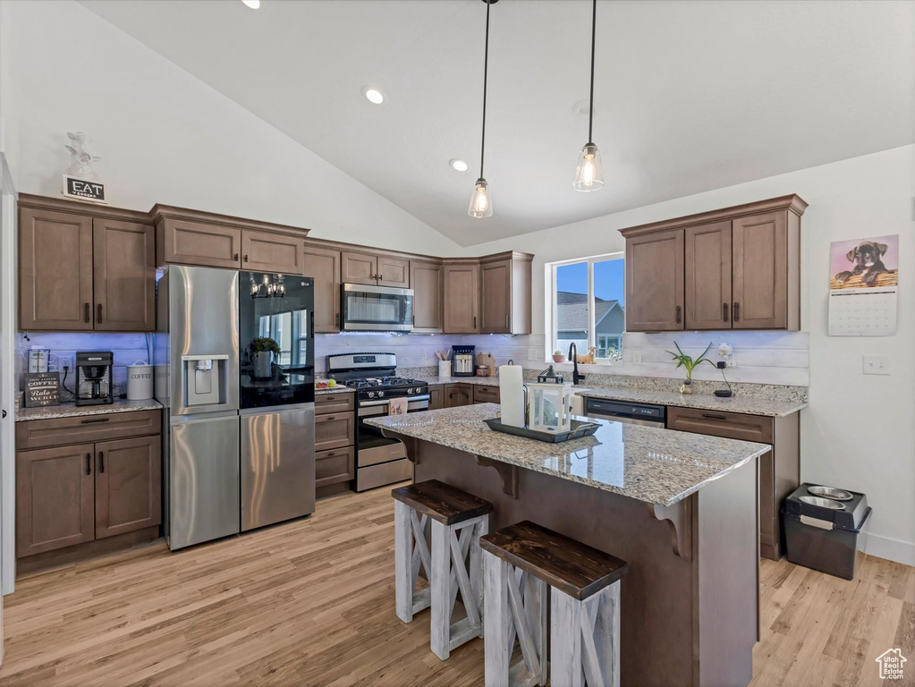 Kitchen with appliances with stainless steel finishes, backsplash, light wood-style floors, recessed lighting, and high vaulted ceiling
