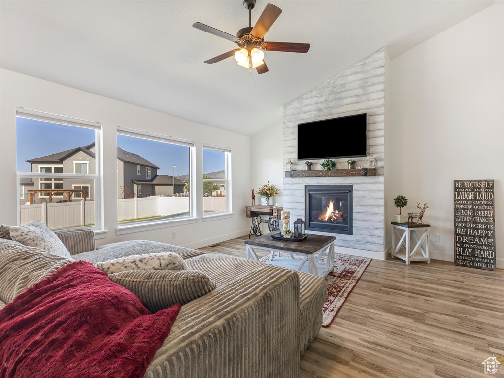 Living area with lofted ceiling, a ceiling fan, wood finished floors, baseboards, and a large fireplace