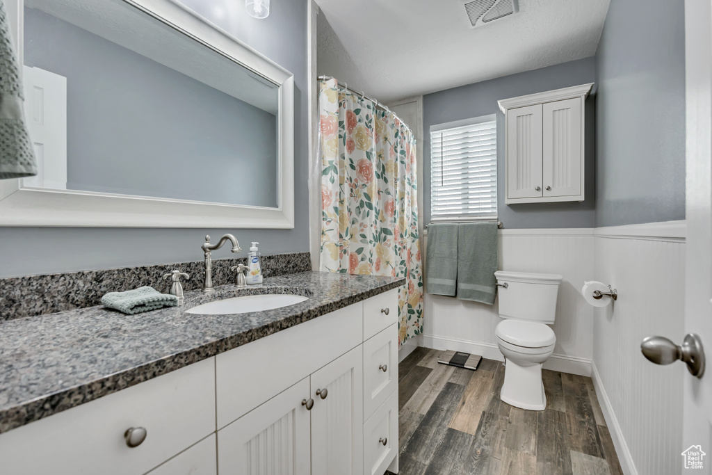 Bathroom with toilet, wood finished floors, vanity, wainscoting, and curtained shower
