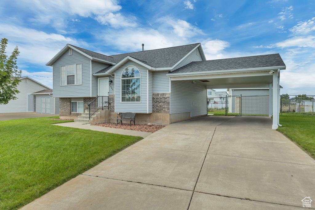 Split level home with a shingled roof, brick siding, concrete driveway, an attached carport, and an outbuilding