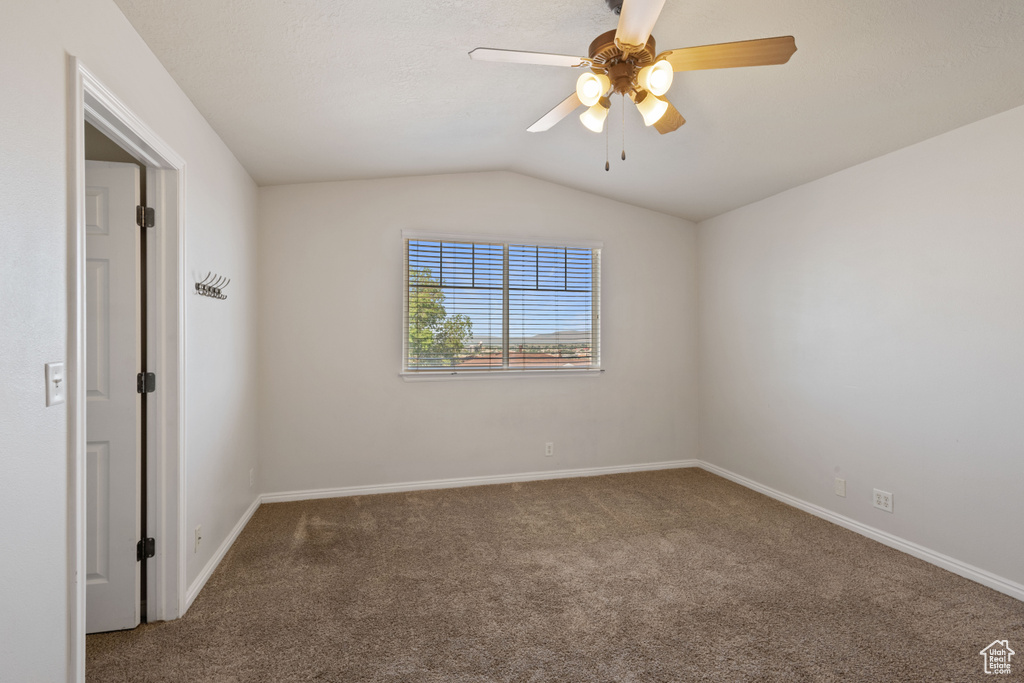 Carpeted spare room with baseboards, vaulted ceiling, and a ceiling fan