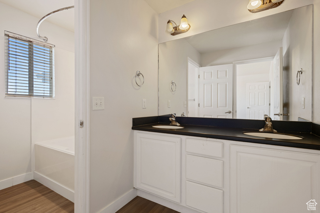 Full bath with wood finished floors, baseboards, double vanity, and a tub