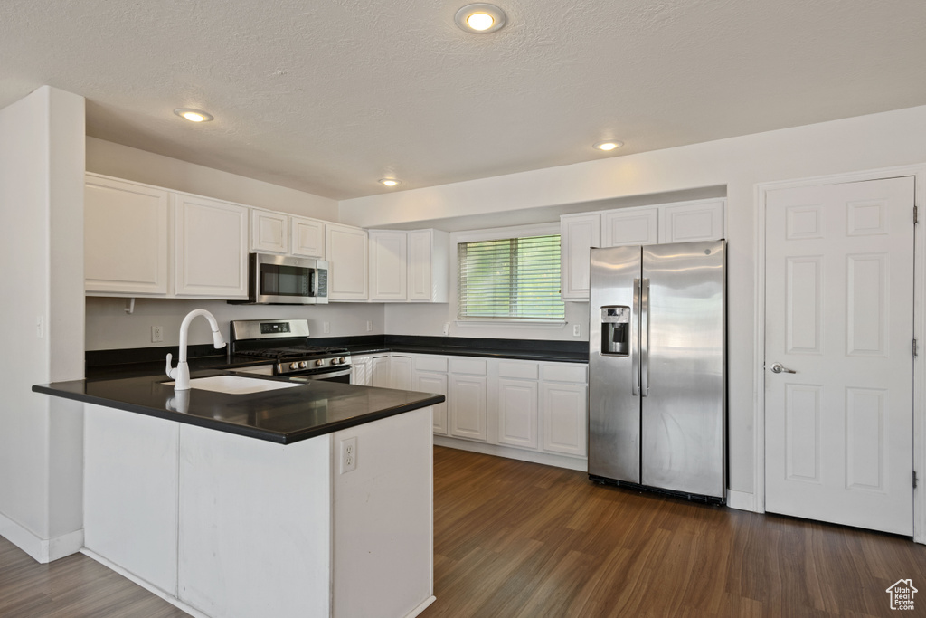 Kitchen featuring appliances with stainless steel finishes, a sink, a peninsula, dark countertops, and white cabinets