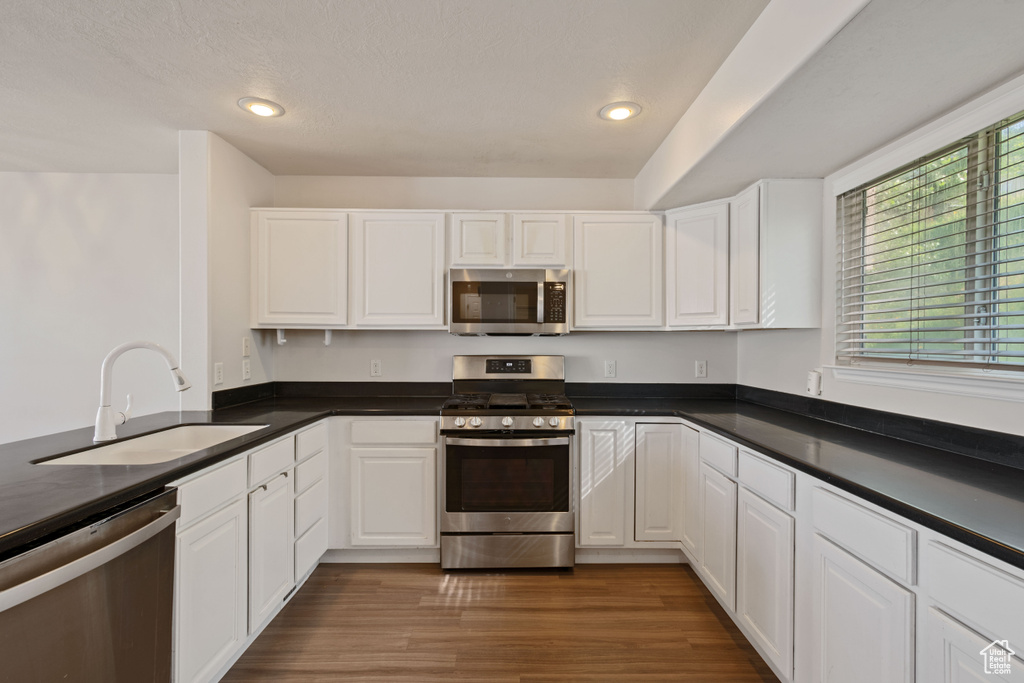 Kitchen with appliances with stainless steel finishes, a sink, dark countertops, white cabinets, and recessed lighting