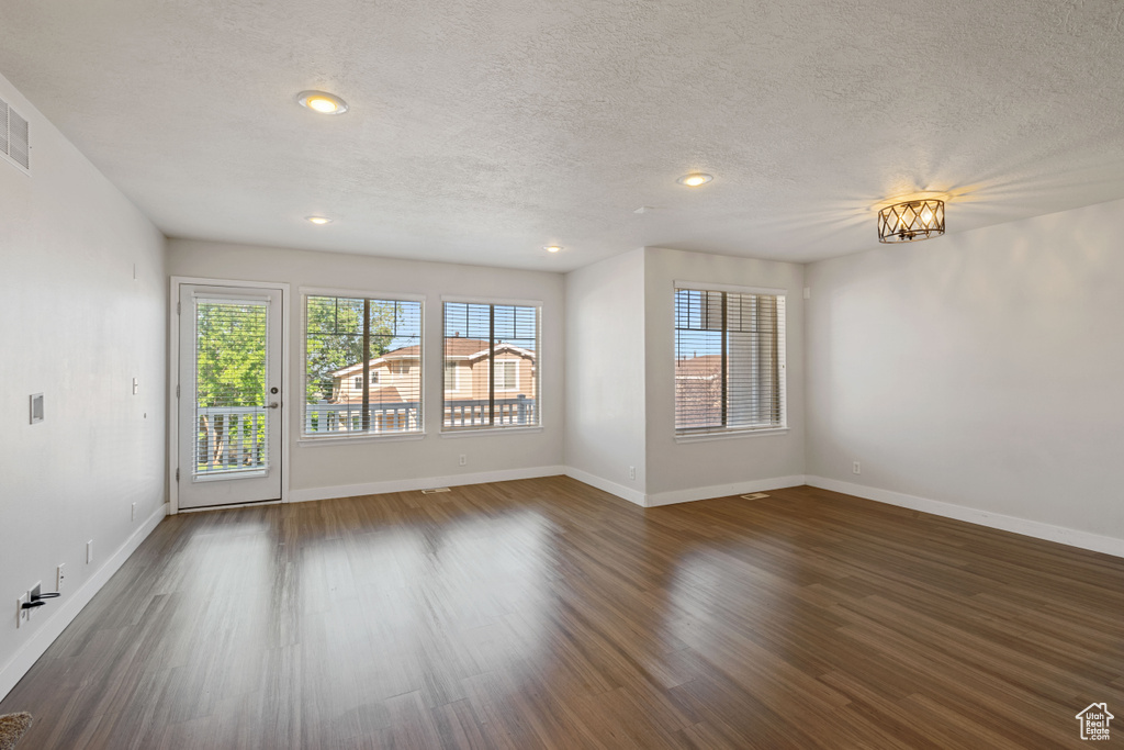 Empty room featuring dark wood finished floors, a textured ceiling, baseboards, and recessed lighting
