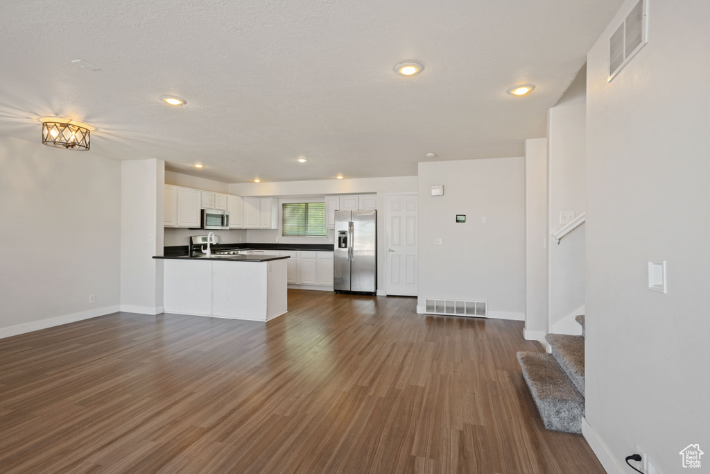 Kitchen with stainless steel appliances, dark countertops, open floor plan, white cabinets, and dark wood finished floors