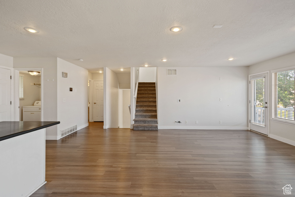 Unfurnished living room featuring washer / dryer, wood finished floors, a textured ceiling, stairway, and baseboards