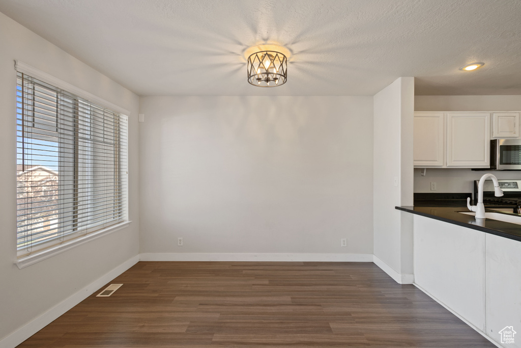 Unfurnished dining area featuring dark wood-style flooring, baseboards, recessed lighting, a sink, and a textured ceiling