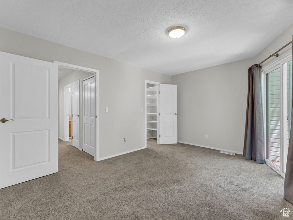 Unfurnished bedroom featuring carpet floors, baseboards, a textured ceiling, and a walk in closet
