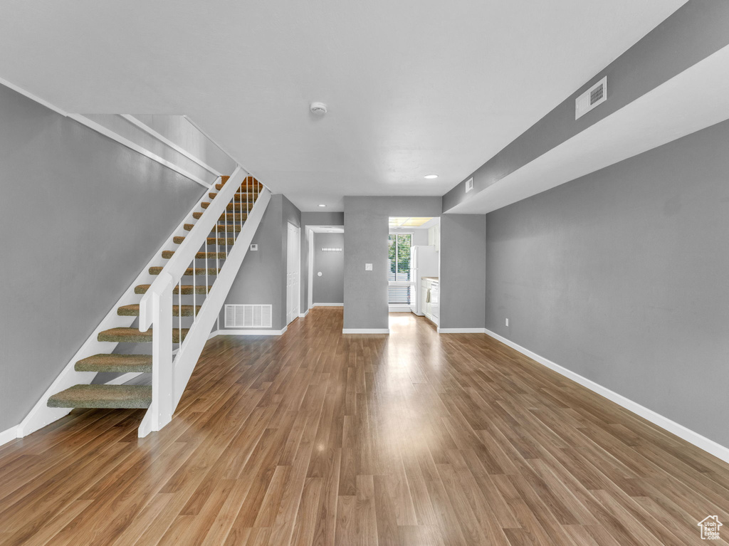 Unfurnished living room featuring stairs, wood finished floors, and baseboards