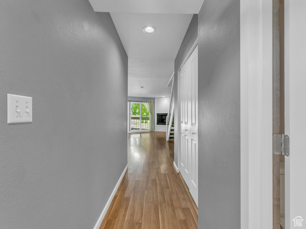 Hallway with baseboards, wood finished floors, a textured wall, and recessed lighting