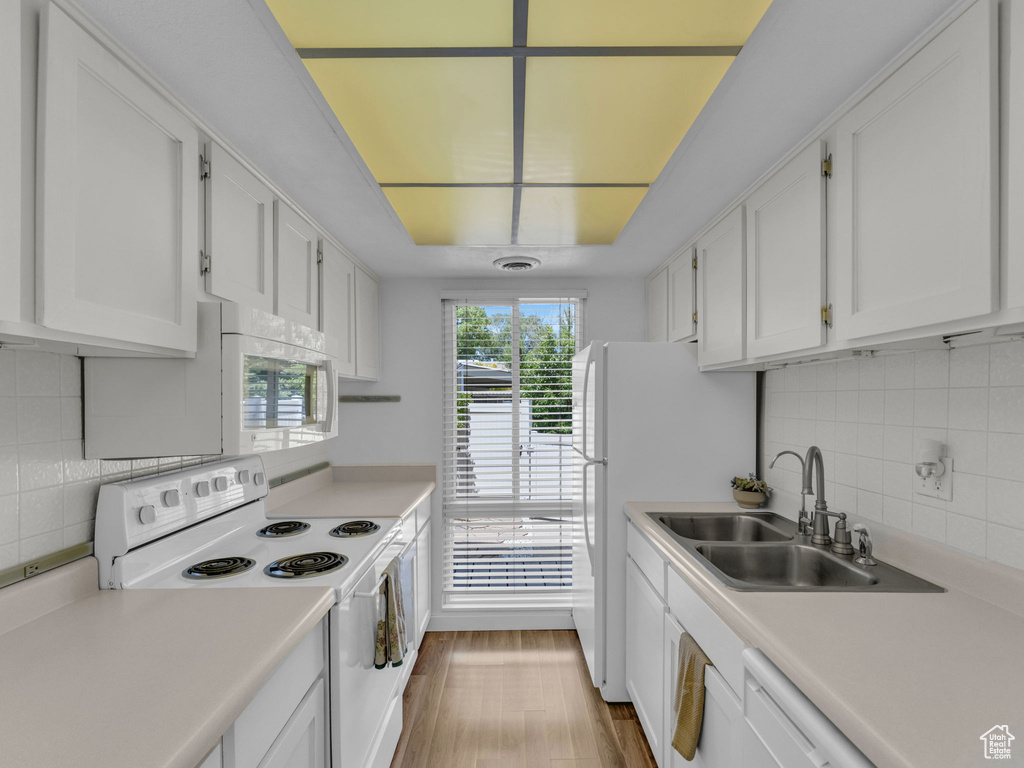 Kitchen featuring white appliances, a sink, white cabinets, and light countertops