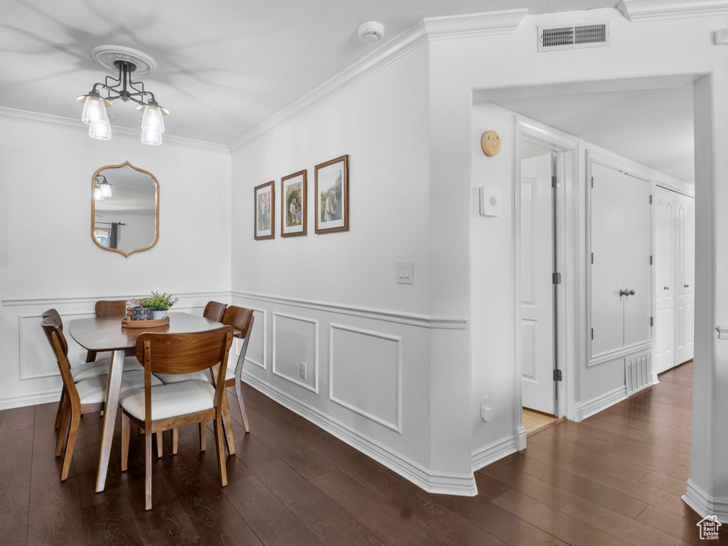 Dining space with dark wood-type flooring, ornamental molding, and a wainscoted wall