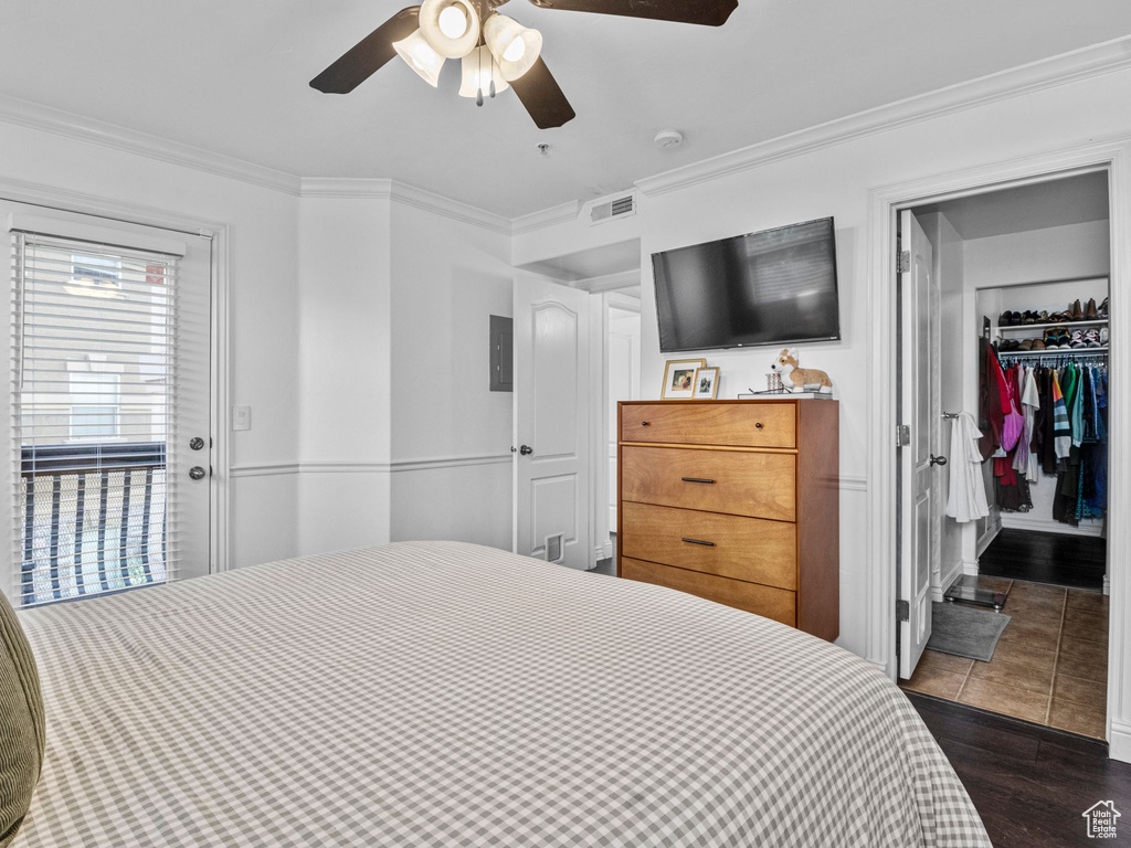 Bedroom featuring ornamental molding, dark wood-type flooring, a ceiling fan, a walk in closet, and electric panel