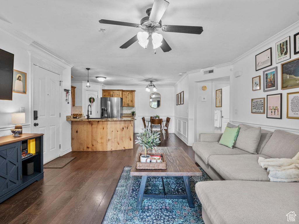 Living room with crown molding, dark wood-type flooring, a ceiling fan, and wainscoting