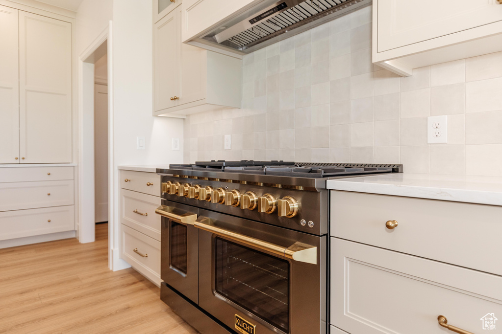 Kitchen featuring double oven range, custom range hood, tasteful backsplash, light wood finished floors, and white cabinets