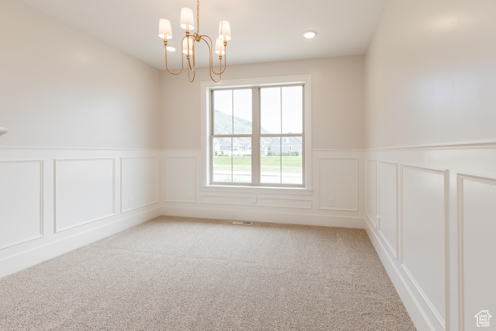 Empty room with a decorative wall, a chandelier, light carpet, a wainscoted wall, and recessed lighting