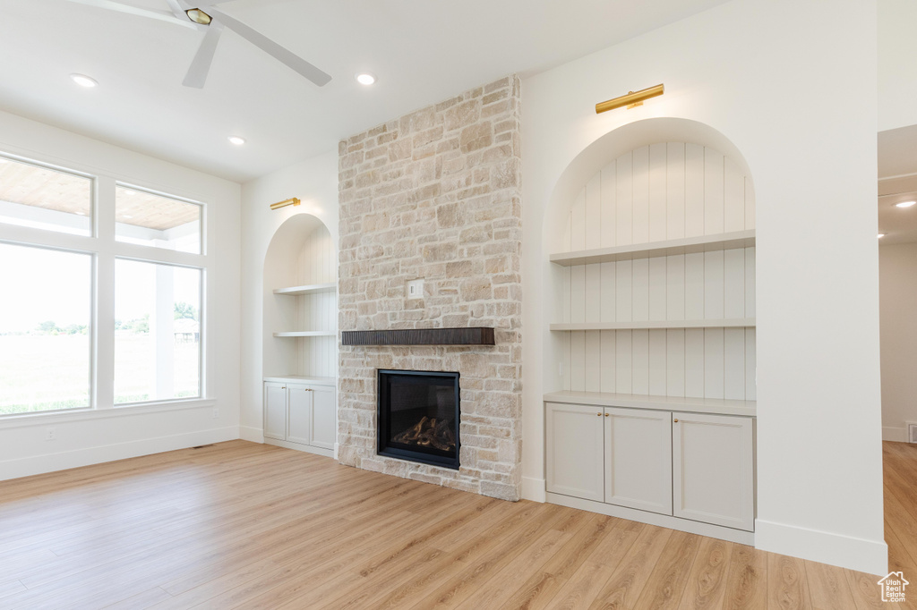 Unfurnished living room featuring ceiling fan, built in features, light wood-style floors, a stone fireplace, and baseboards