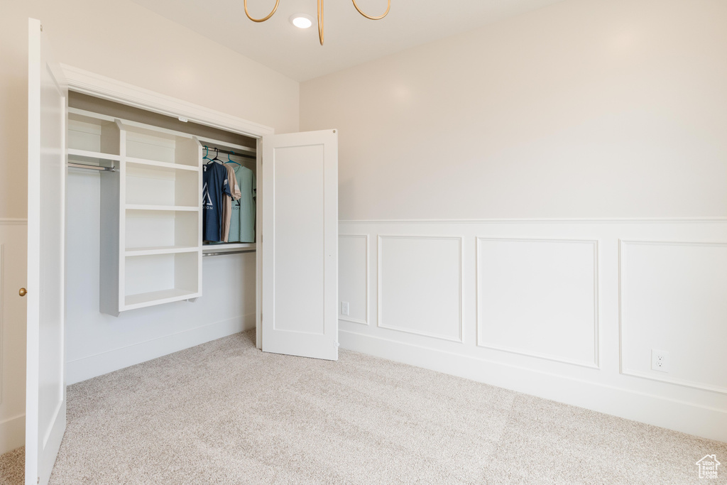 Unfurnished bedroom featuring carpet, a chandelier, a decorative wall, wainscoting, and a closet