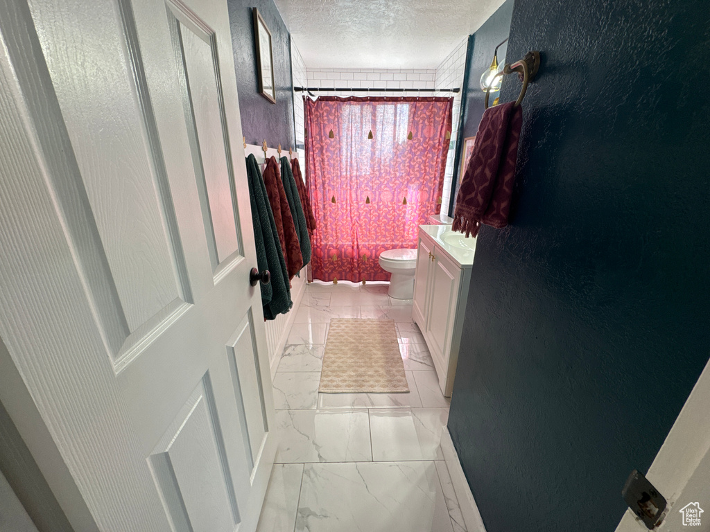 Full bath featuring vanity, toilet, a textured ceiling, marble finish flooring, and shower / bath combo