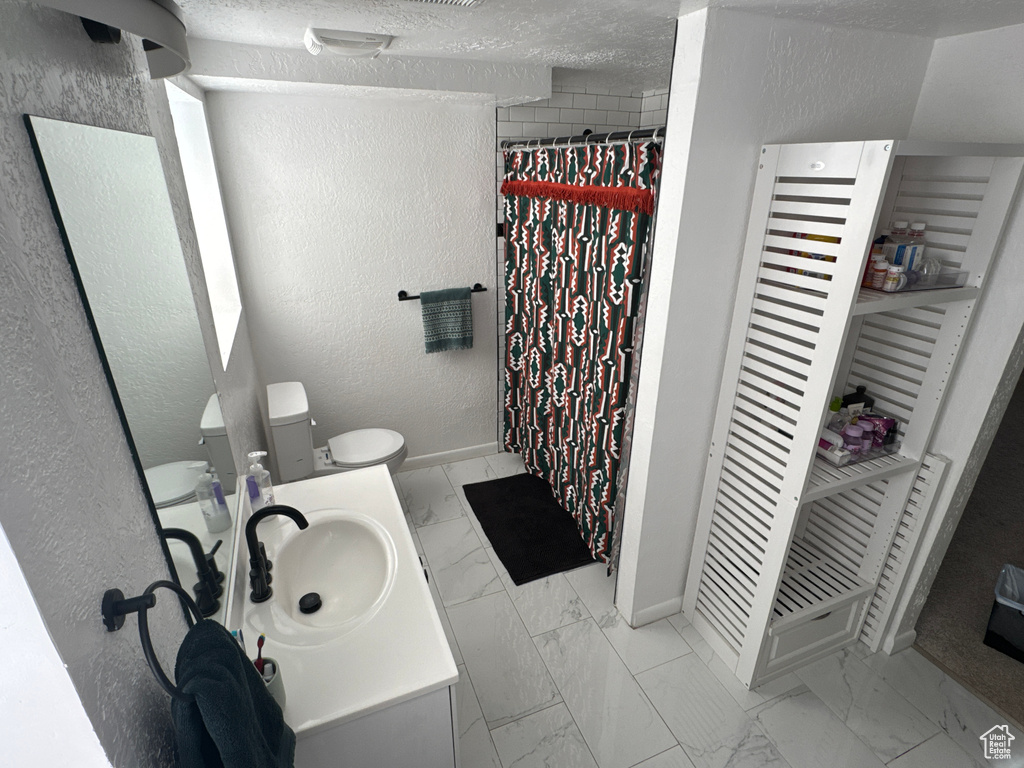 Bathroom featuring marble look tile flooring, baseboards, toilet, a textured wall, and vanity