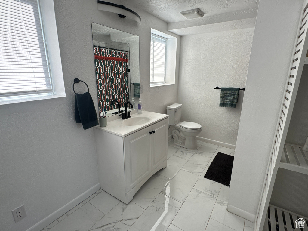 Bathroom featuring baseboards, marble look tile flooring, vanity, toilet, and a textured wall