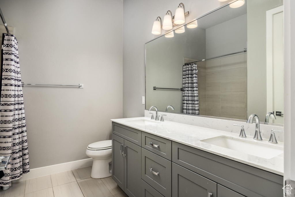 Bathroom with toilet, double vanity, baseboards, and a shower with shower curtain