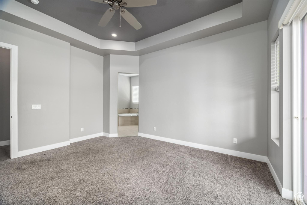 Unfurnished bedroom with carpet flooring, a tray ceiling, baseboards, ensuite bathroom, and recessed lighting